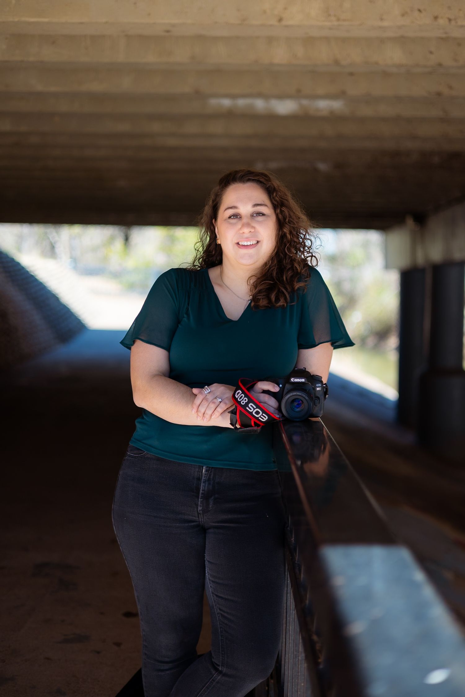 Samantha Calverley in a emerald green top stands under a concrete structure in natural lighting.
