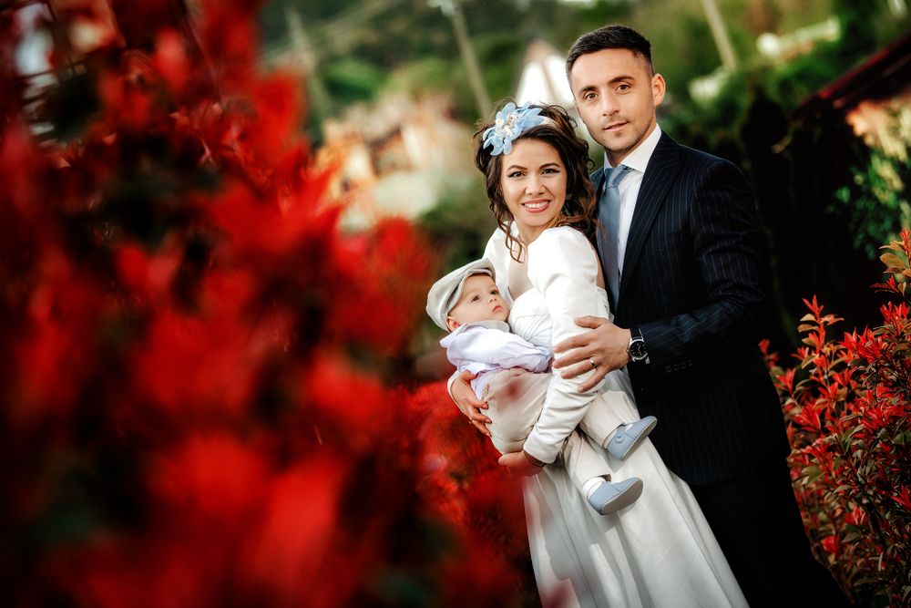 A newlywed couple embraces in a garden with vibrant red fall foliage creating a romantic frame.