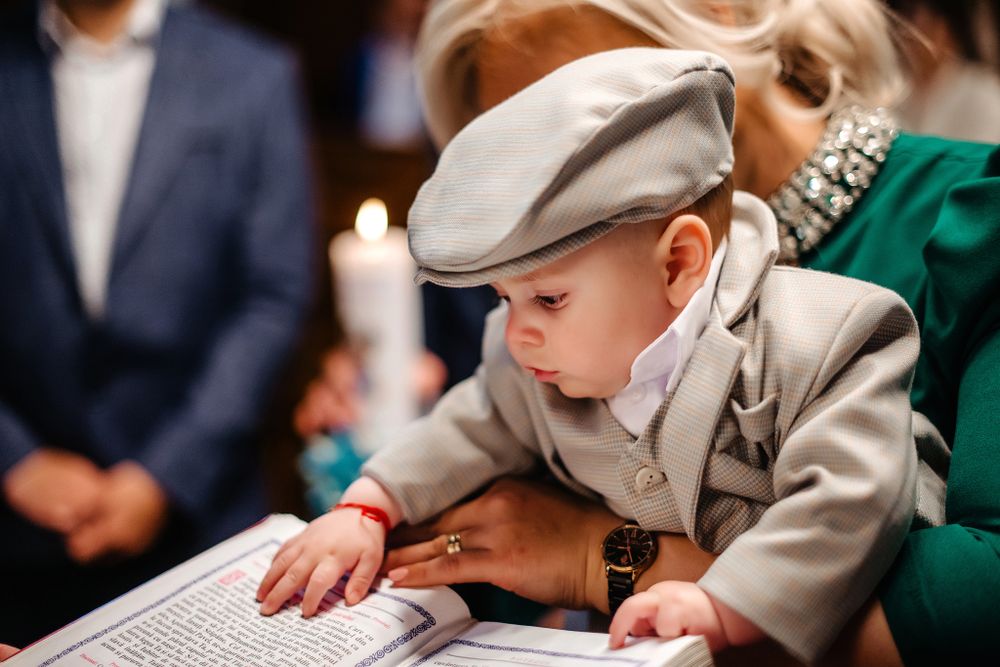 A young boy in a gray newsboy cap and suit leans over to examine what appears to be a book.