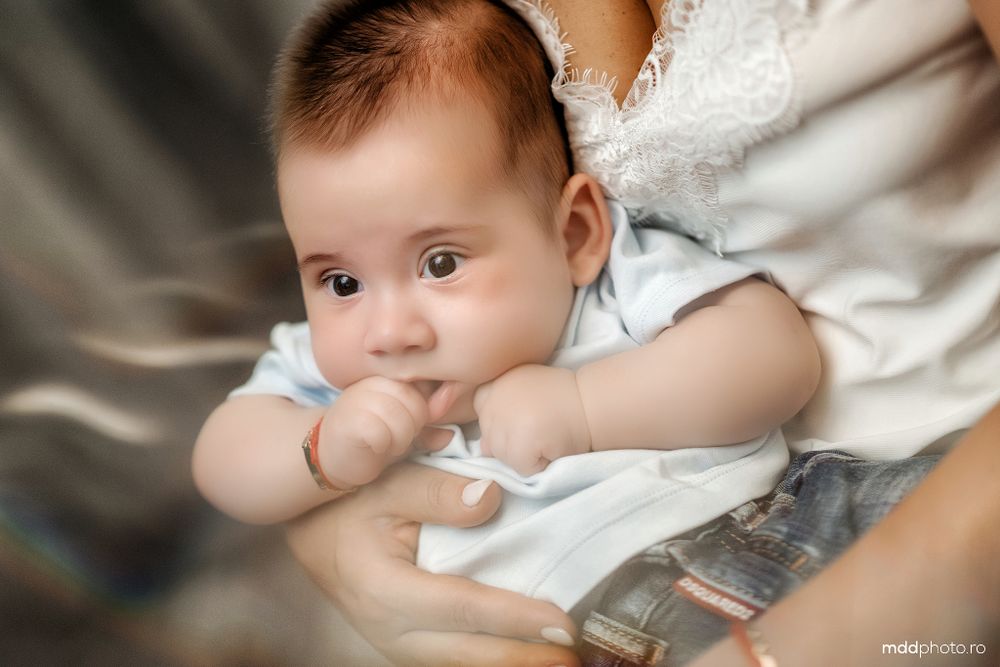 Baby in blue clothing laying on a white blanket while gazing upward with a thoughtful expression.