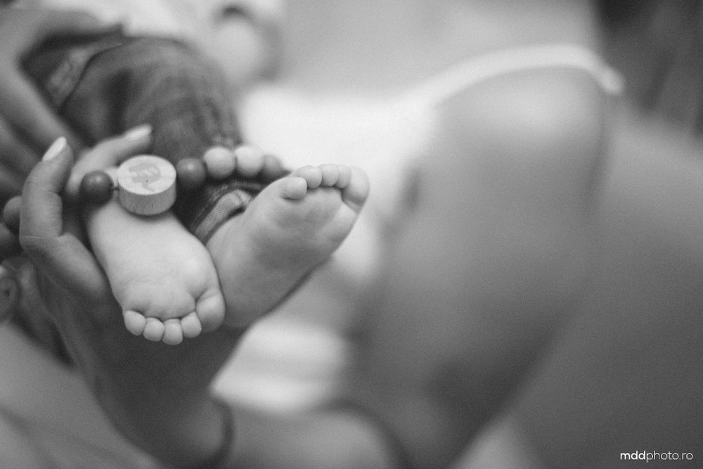 Black and white close-up photograph of tiny newborn baby feet with parent's hand holding a small coin for size comparison.