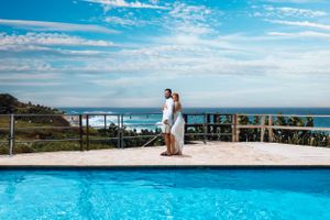 Couple standing by infinity pool overlooking ocean view at luxury resort.