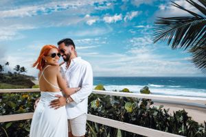 Romantic beach scene with couple embracing on balcony overlooking tropical coastline.