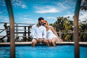 Couple sits intimately at the edge of an infinity pool overlooking tropical scenery.