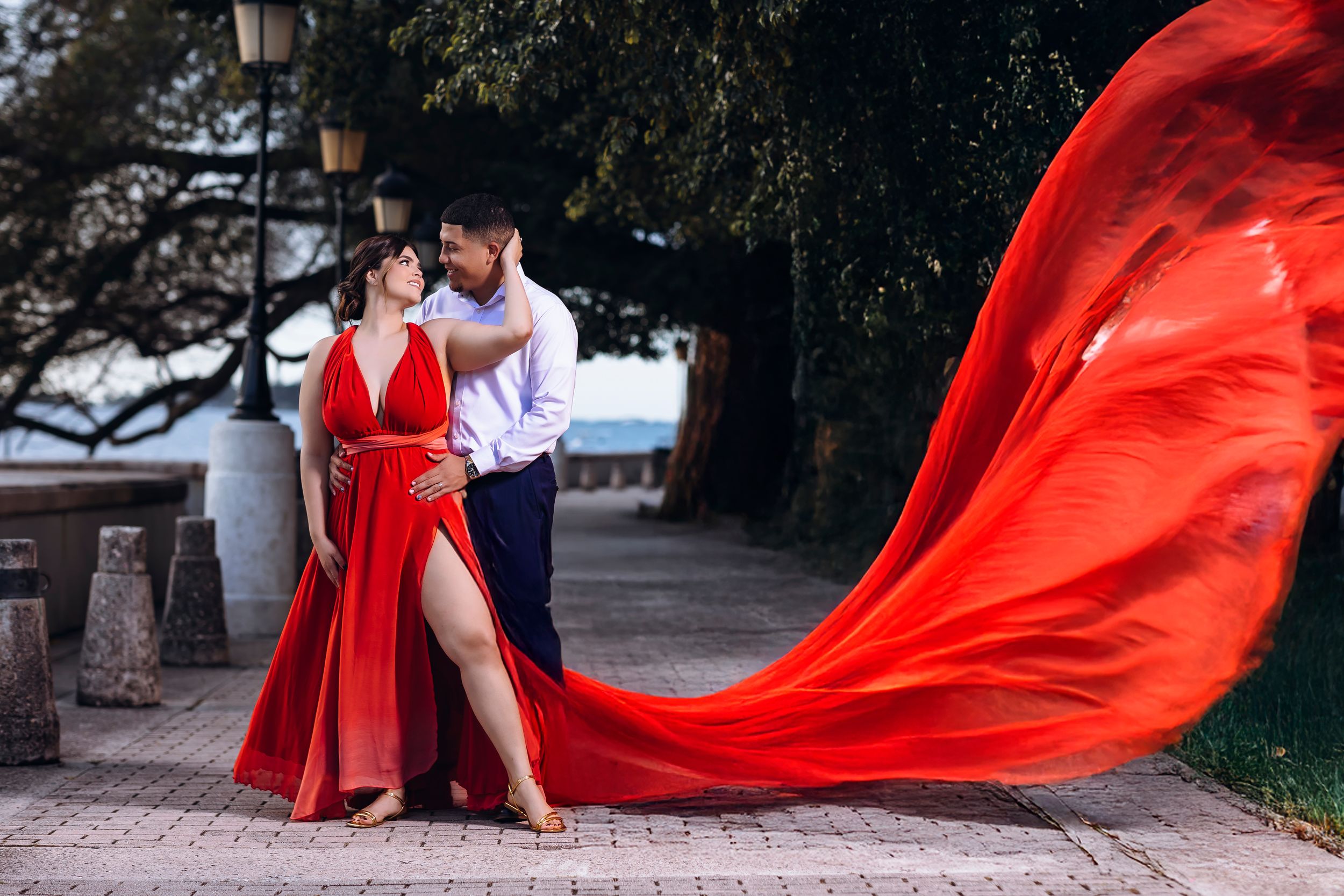 A flowing red dress billows dramatically in the wind during an outdoor photo session at dusk.