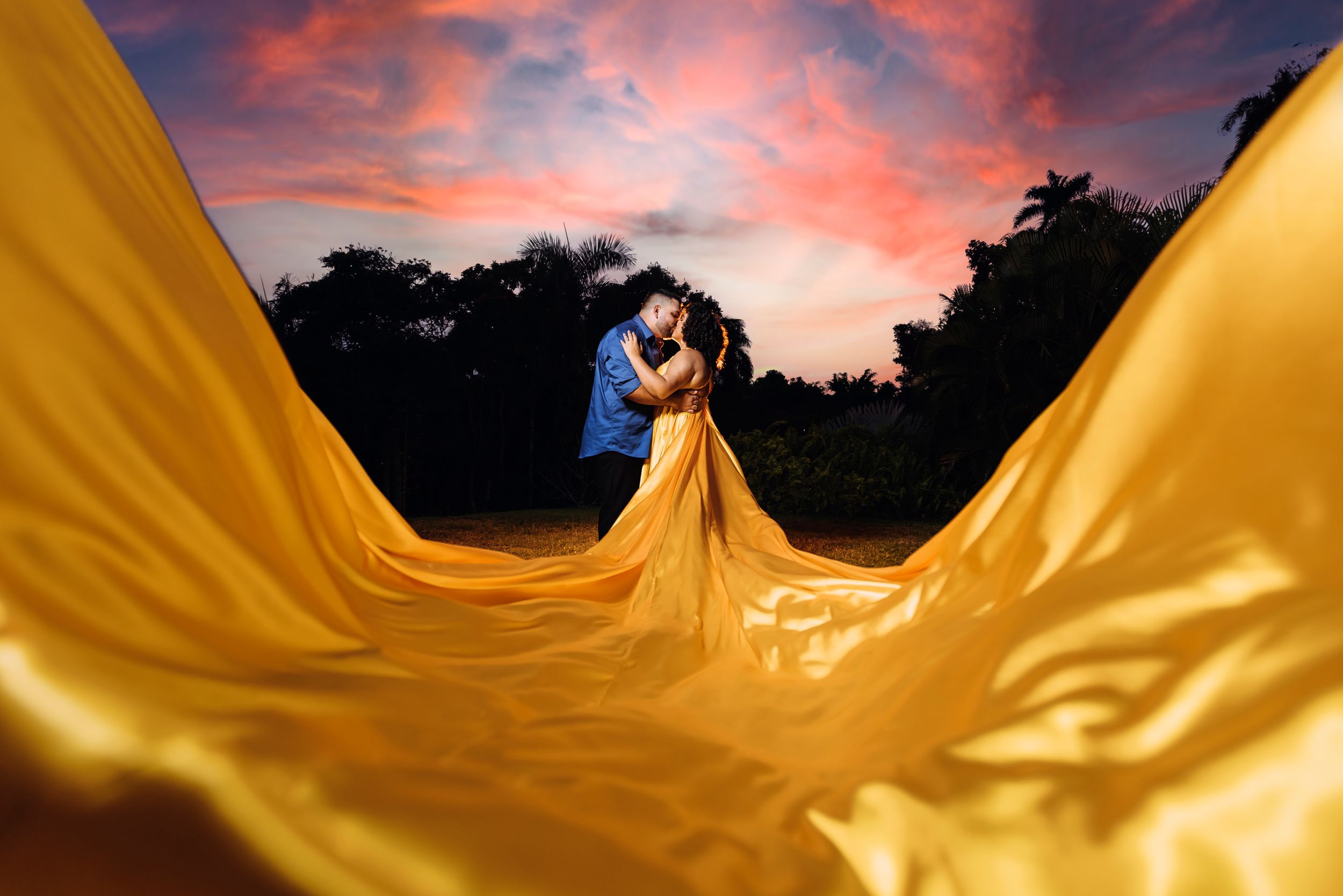 A dramatic sunset photoshoot featuring flowing yellow fabric against a purple sky.