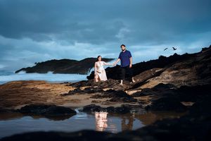 A couple embraces on rocky coastal cliffs during a moody blue sunset by the ocean.