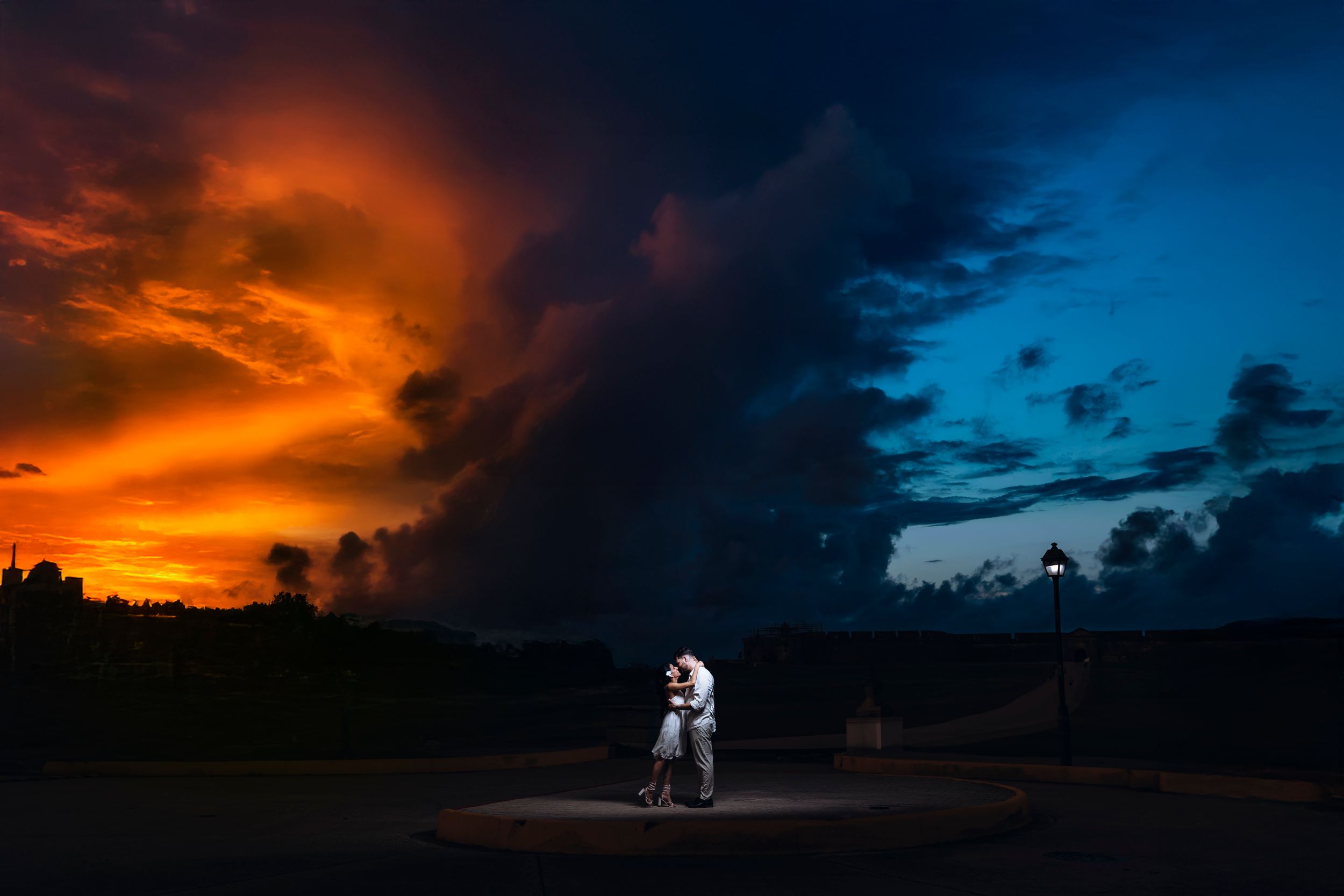 Single spotlight illuminates dancing couple against stunning split sunset and stormy sky.