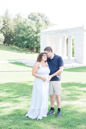 A couple poses playfully on a grassy lawn in front of white columns while taking outdoor engagement photos.