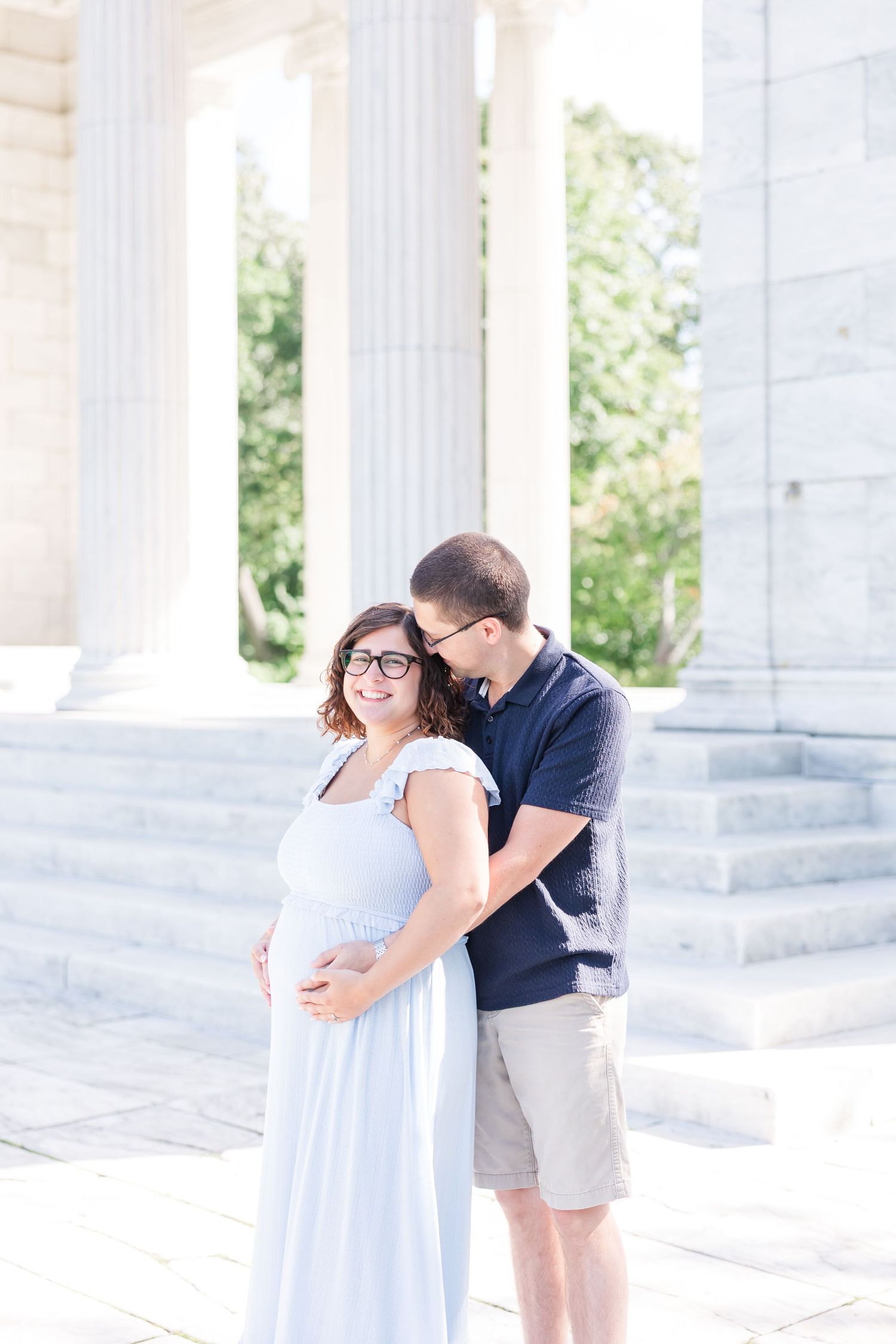Couple shares romantic moments in a bright white columned outdoor setting during a photography session.