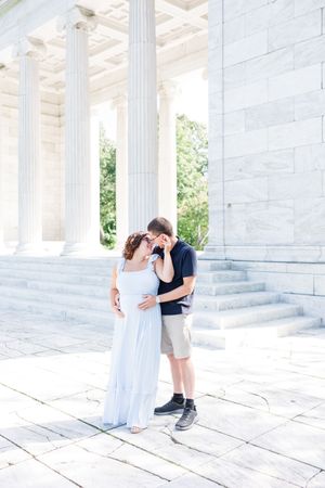 A romantic couple shares tender moments among white marble columns at a historic architectural landmark during a photo session.