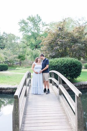 Couple sharing a romantic moment on a white wooden footbridge over a tranquil pond surrounded by lush greenery.