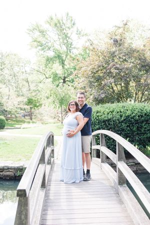 A romantic couple enjoys a peaceful moment together on a white wooden bridge surrounded by lush greenery.