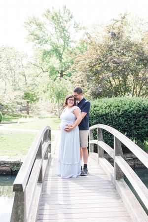 A couple shares intimate moments on a white wooden footbridge surrounded by lush greenery in a peaceful garden setting.