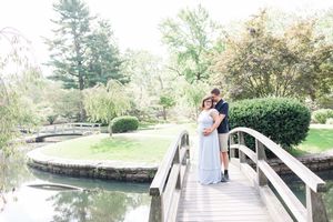 A couple in wedding attire stands on a wooden bridge over a serene garden pond surrounded by lush greenery.