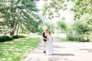 A romantic couple walks together along a tree-lined gravel path in a scenic park setting.
