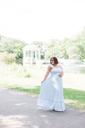 A flowing white maxi dress catches the sunlight in a park setting with a white gazebo in the background.