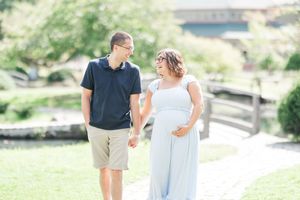 A couple walks hand in hand on a stone path through a lush green garden setting in romantic engagement photos.