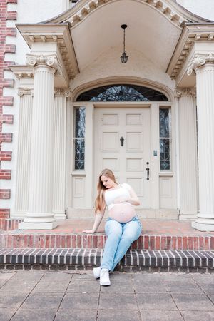 Person poses on the steps of an elegant historic building with white columns and ornate architectural details.