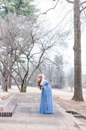 A maternity photoshoot along a stone path surrounded by bare winter trees.