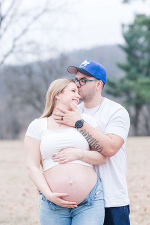Loving maternity photo session in a field showing tender moments between an expecting couple in white tops and jeans.