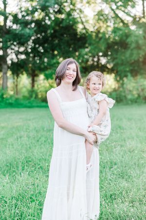 A tender family moment captured in a grassy field wearing white outfits during golden hour.