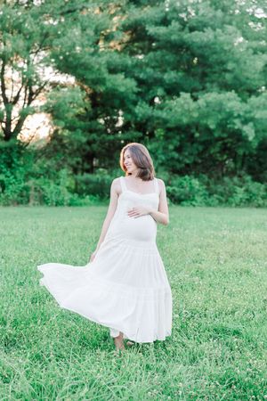 Person in flowing white dress spins gracefully in a sunlit green meadow on a summer day.