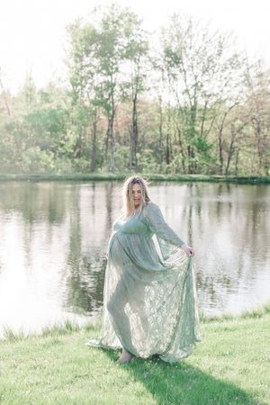 A dreamy figure in a flowing mint green dress dances gracefully by a serene lake surrounded by spring trees.