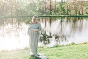 Person wearing a flowy white dress walks gracefully along a serene lakeside path surrounded by spring greenery.