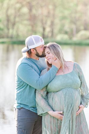 Romantic maternity photo session shows couple in matching blue outfits sharing tender moments by a lake.