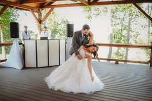 A couple shares their first dance in a rustic covered outdoor venue with wooden beams.