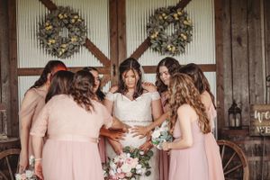 Wedding party in pink dresses posing together outdoors near rustic barn.