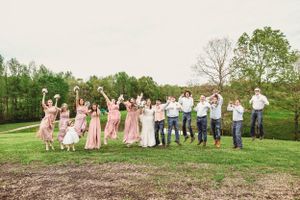 Large wedding party group photo taken in a scenic field during spring.