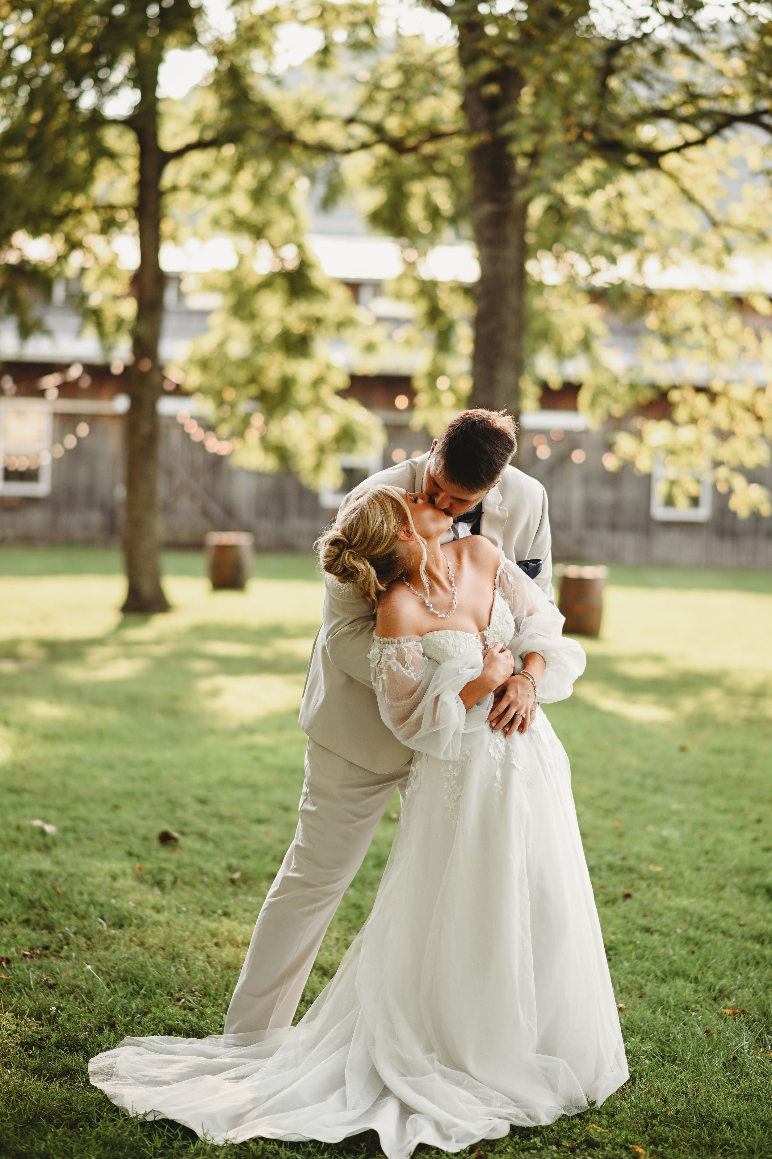 A romantic wedding photoshoot in a sunlit garden with the couple embracing in flowing white dress and light suit.