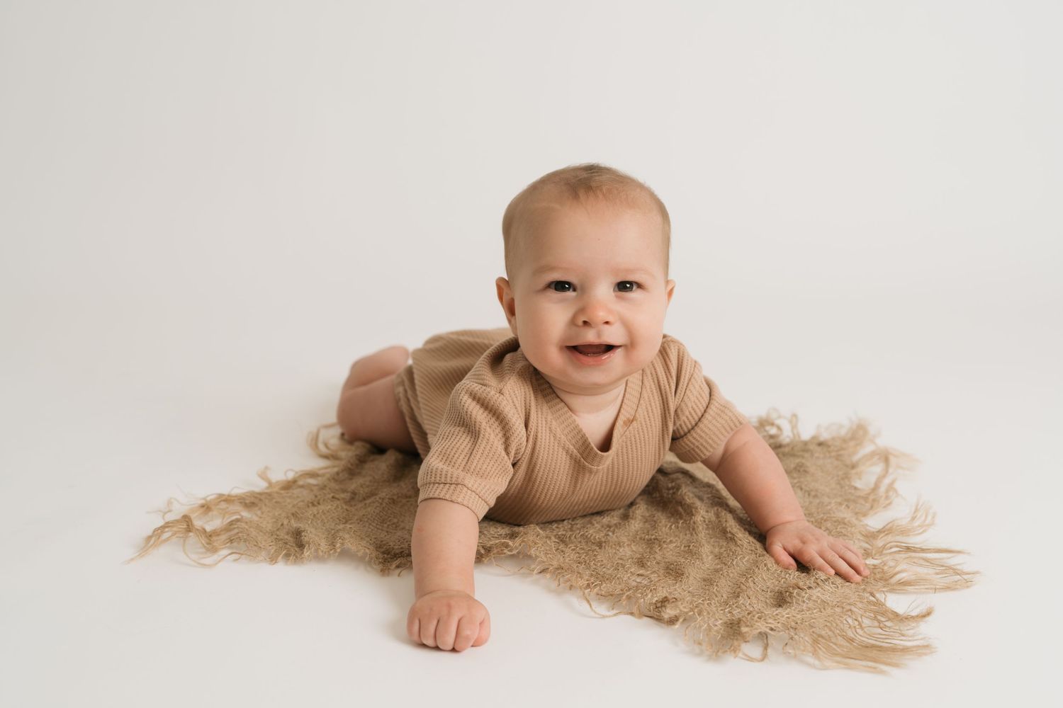 A happy baby lies on a soft beige blanket with a joyful expression and natural lighting.