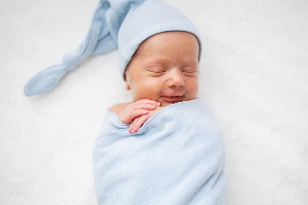 Peaceful baby swaddled in soft blue blanket sleeping on white background.
