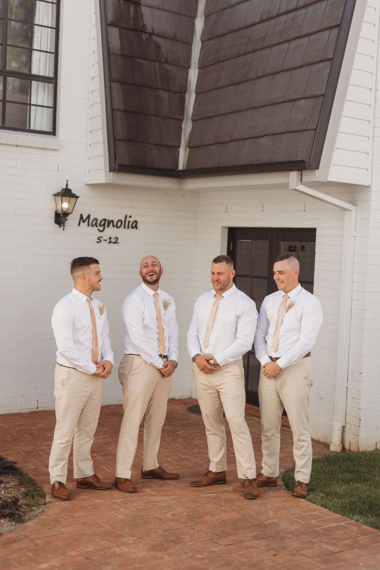 Groomsmen in matching white shirts and khaki pants pose outside The Magnolia venue.