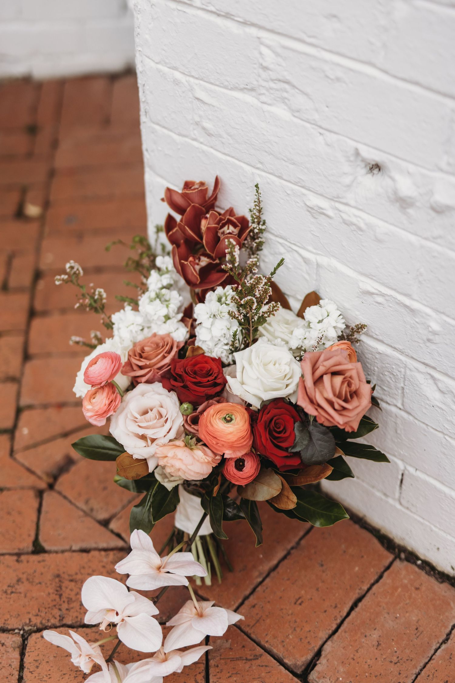Red, pink and white rose bouquet with ranunculus against white painted wall on brick patio.