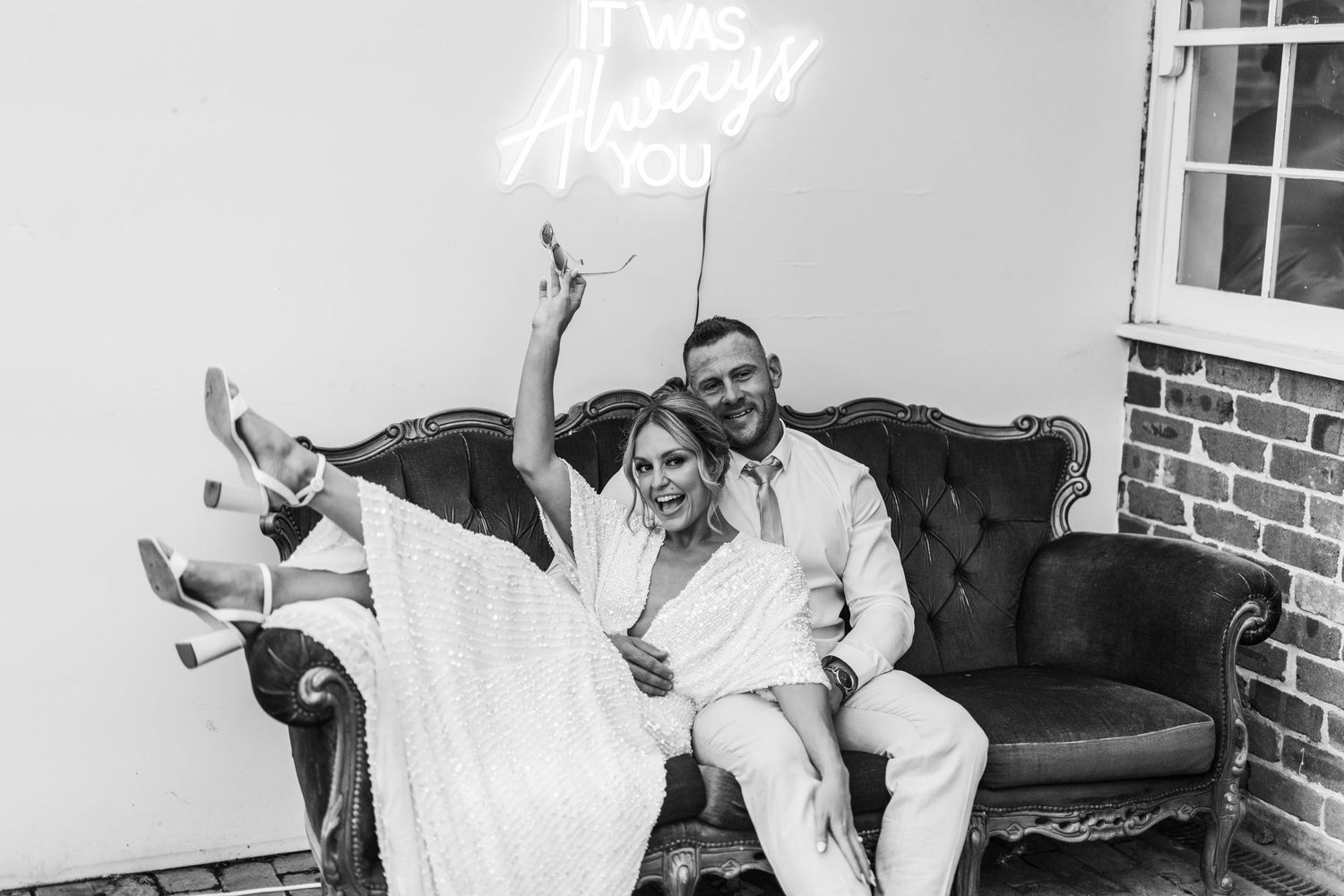 Wedding couple having fun on a vintage brown couch under neon lighting.