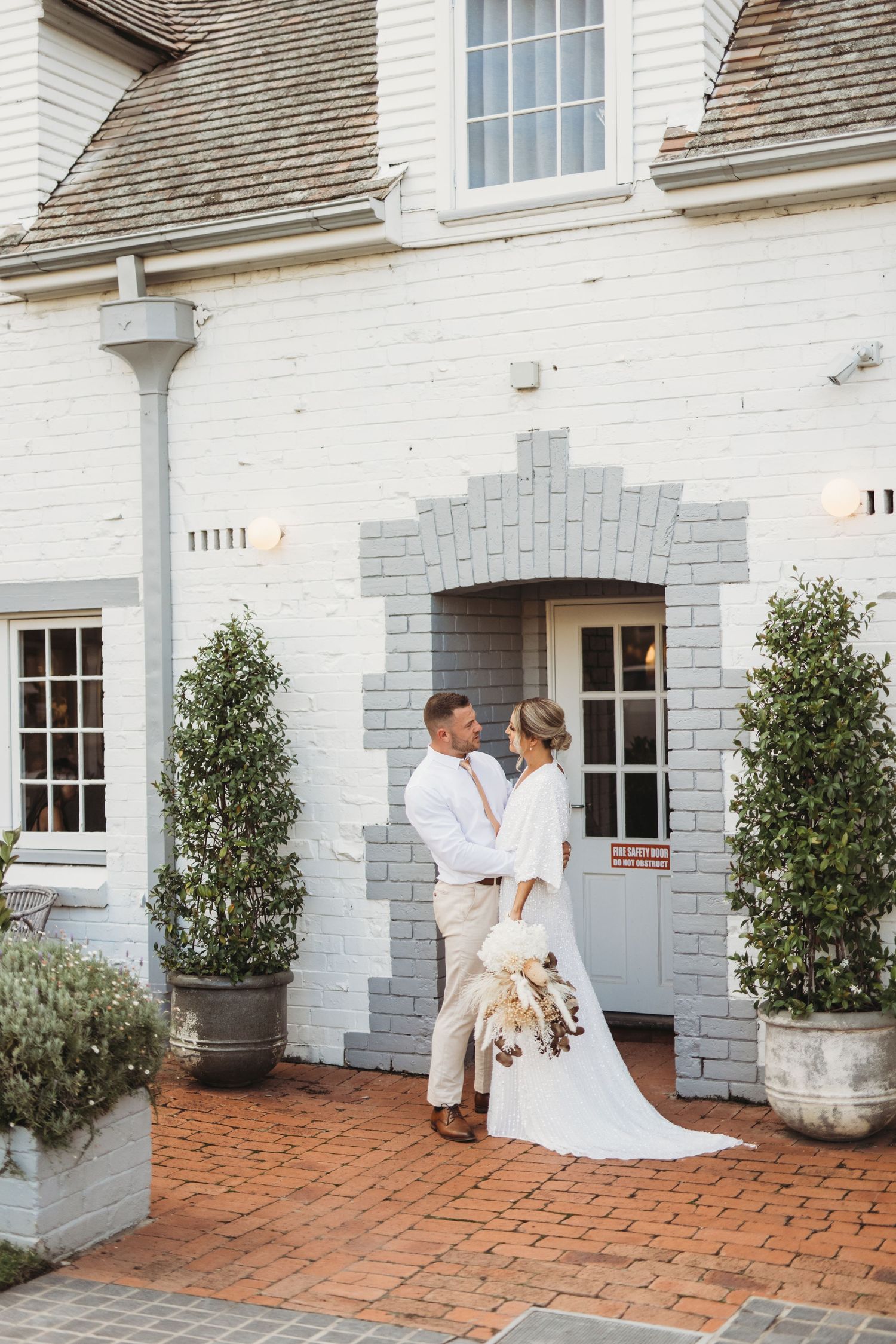 A romantic wedding portrait in front of a white brick building entrance.