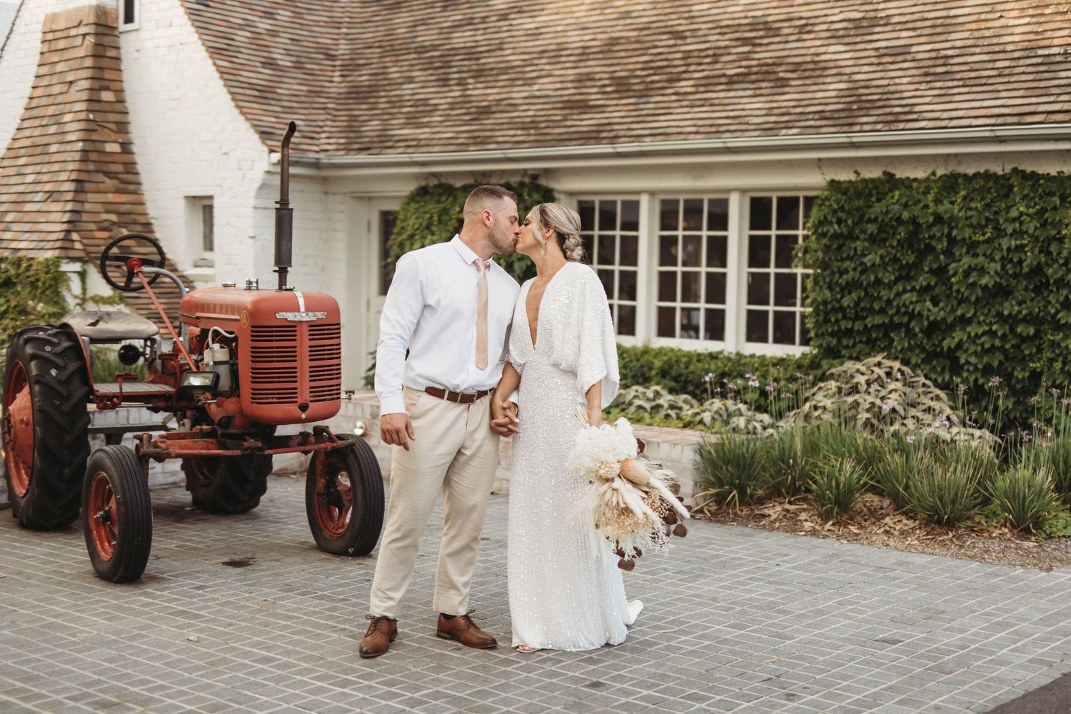 Newlyweds share an intimate moment next to a vintage red tractor.
