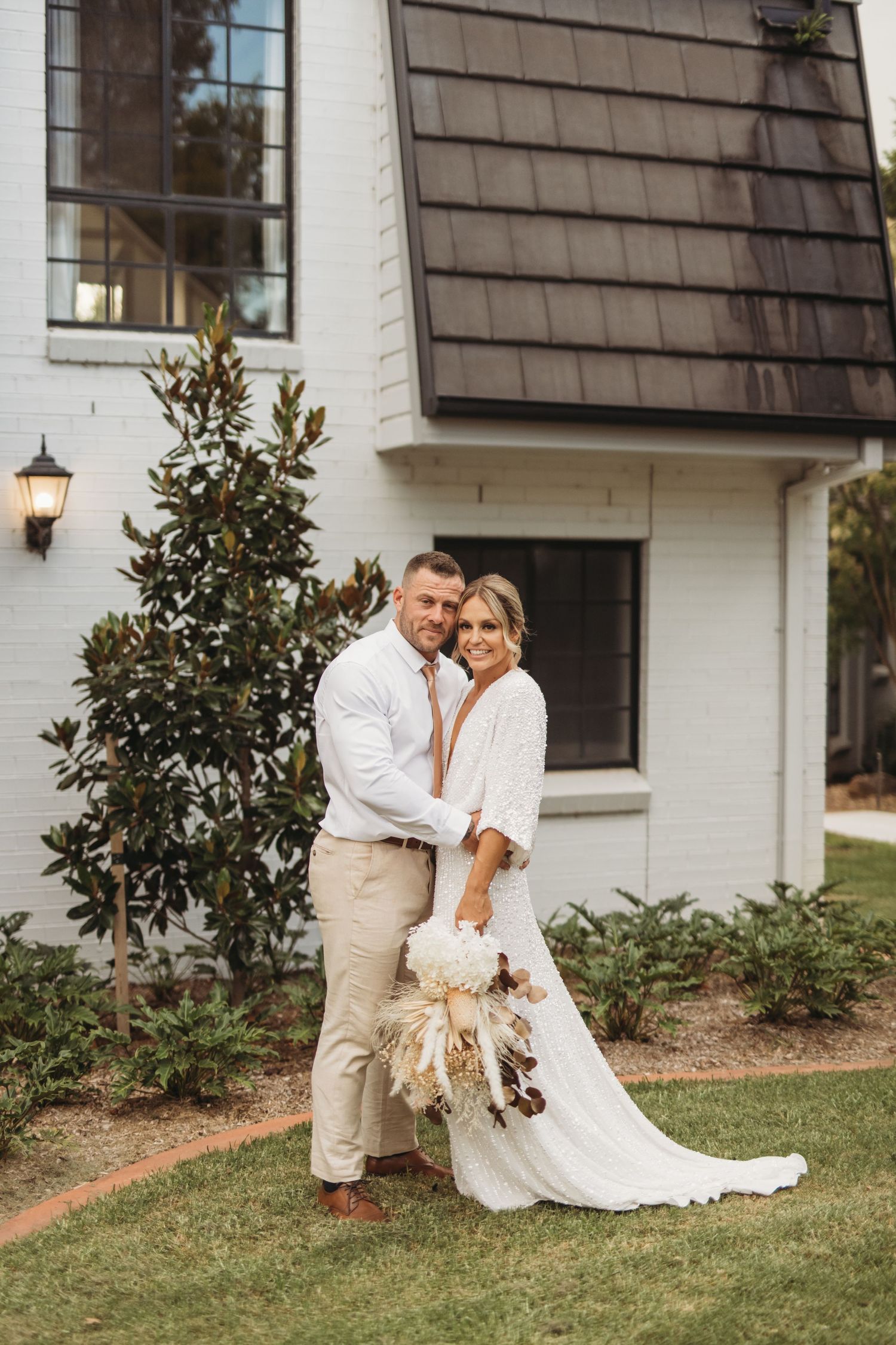 Romantic wedding portrait in front of a white building with dark shutters and magnolia tree.