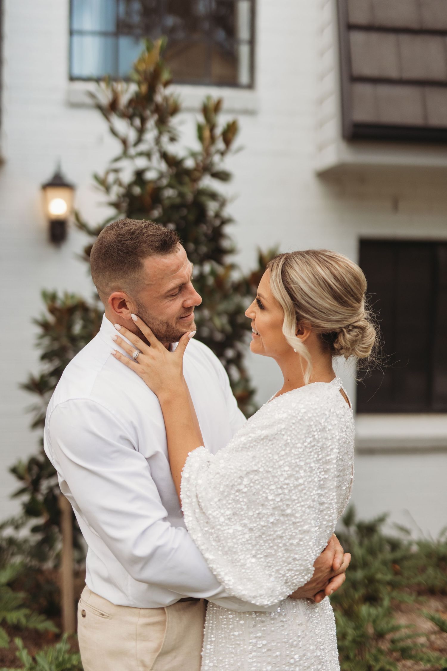 Intimate wedding portrait against white building with magnolia tree and lantern.