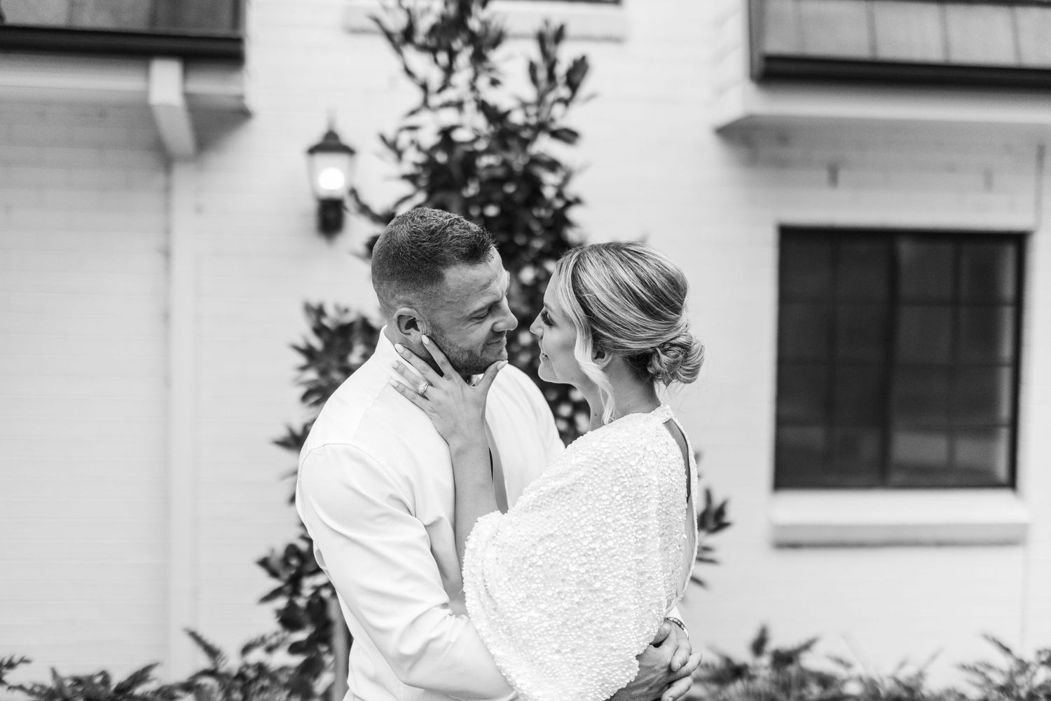 Black and white romantic portrait of couple in wedding attire against white building.
