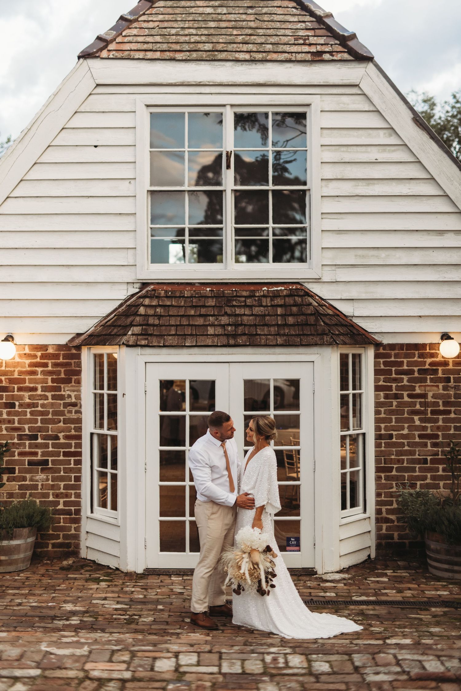 Newlyweds pose outside a charming brick and white colonial style building with French doors.