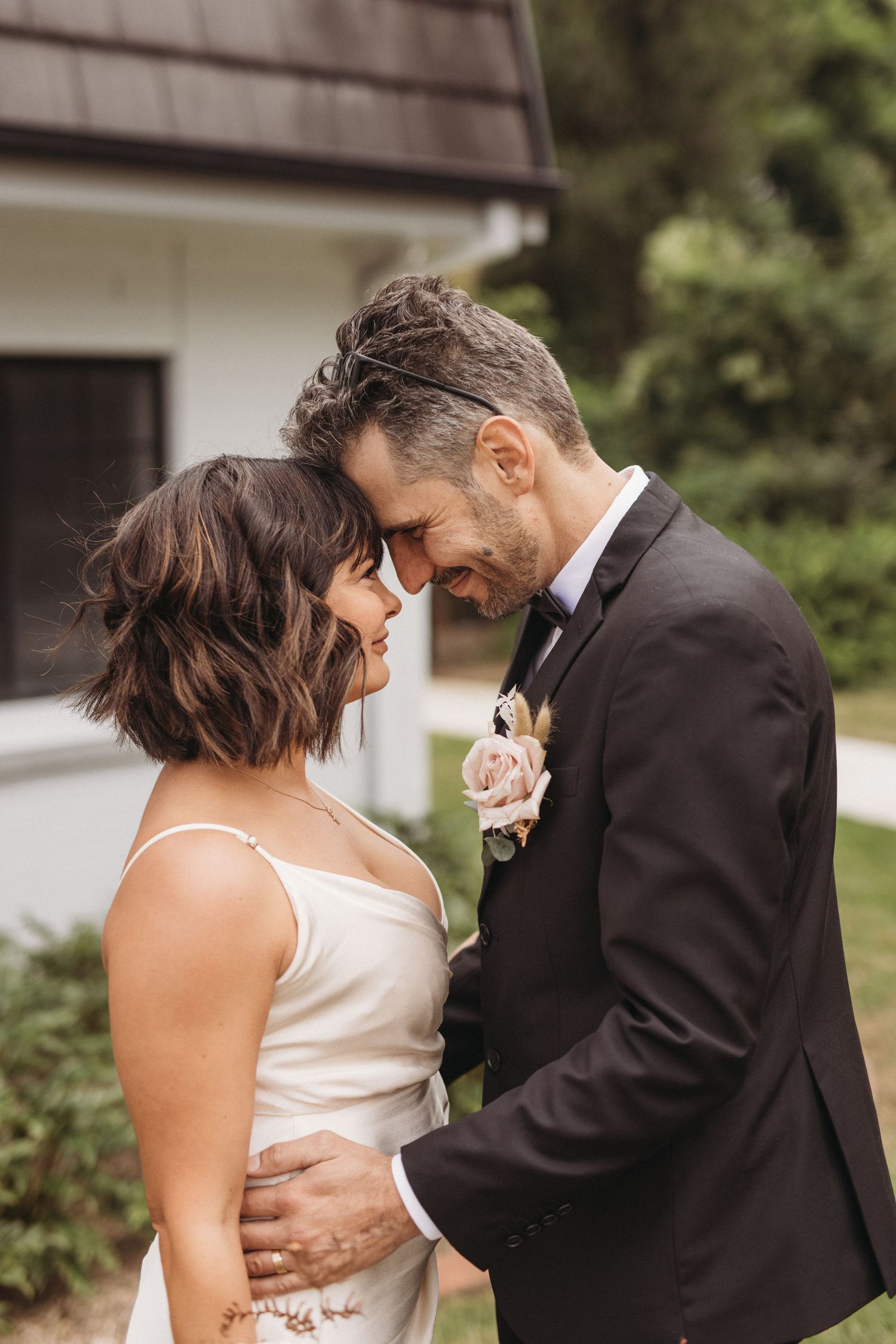 Intimate wedding portrait of couple sharing tender moment outside white building.