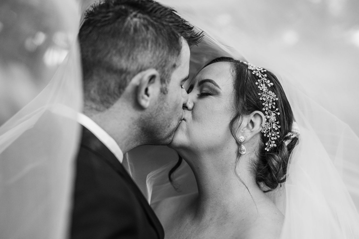 An intimate black and white wedding portrait capturing a tender kiss between newlyweds.