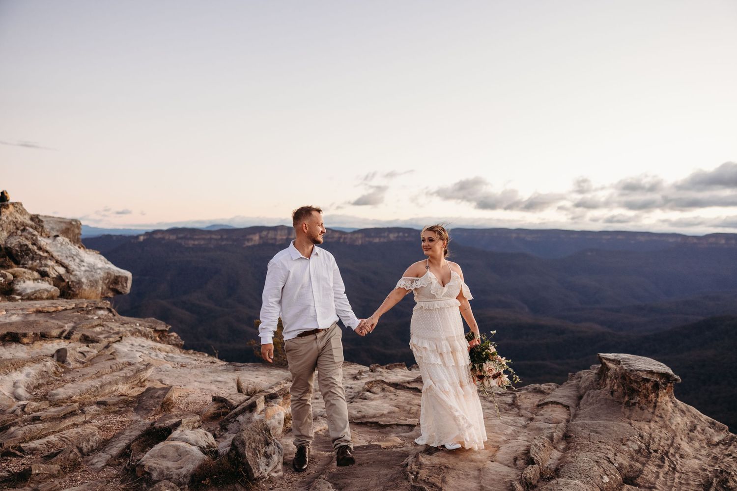 Newlyweds stand together on a rocky mountain overlook at sunset.