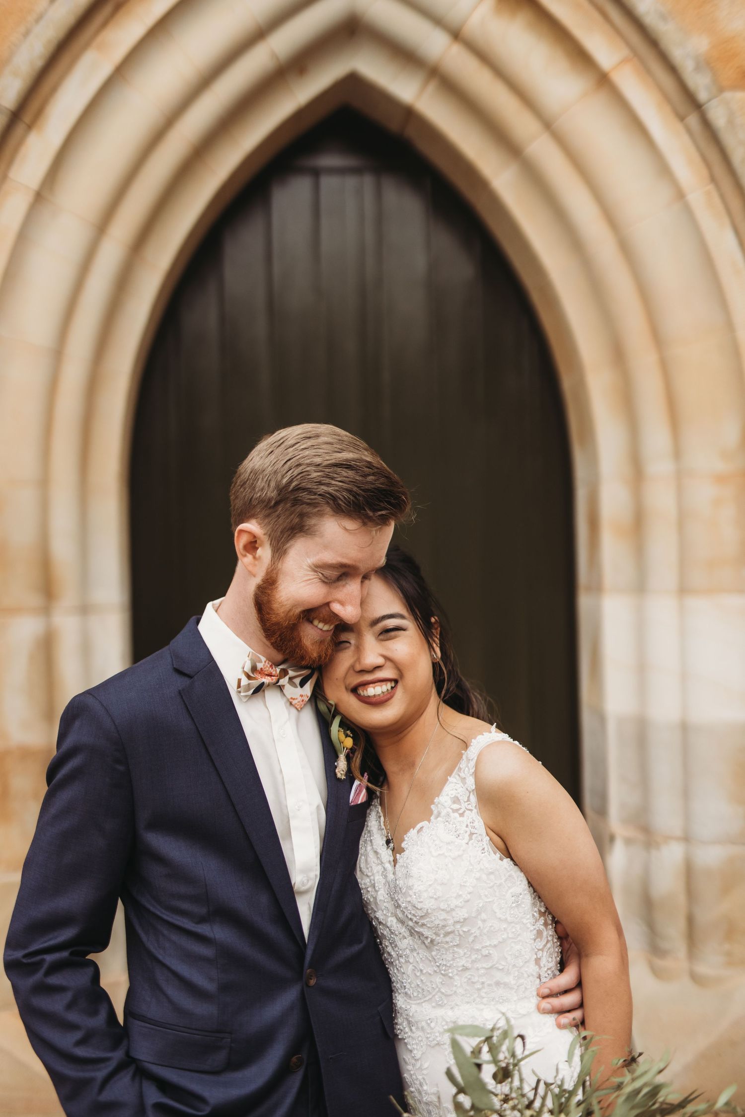 Newlyweds share an intimate moment in front of a gothic church archway.