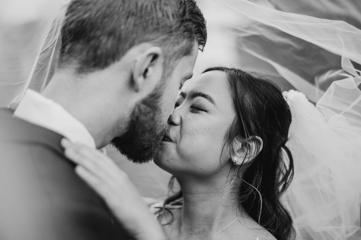 A romantic black and white portrait of a couple sharing an intimate moment under a bridal veil.